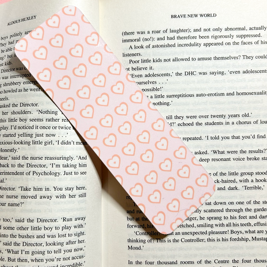 Pink heart-patterned bookmark laid across the pages of an open book.