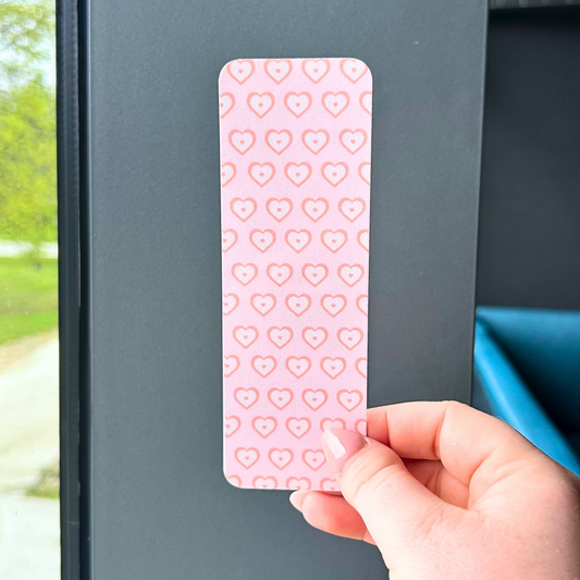 Pink heart-patterned bookmark in front of window and gray wall